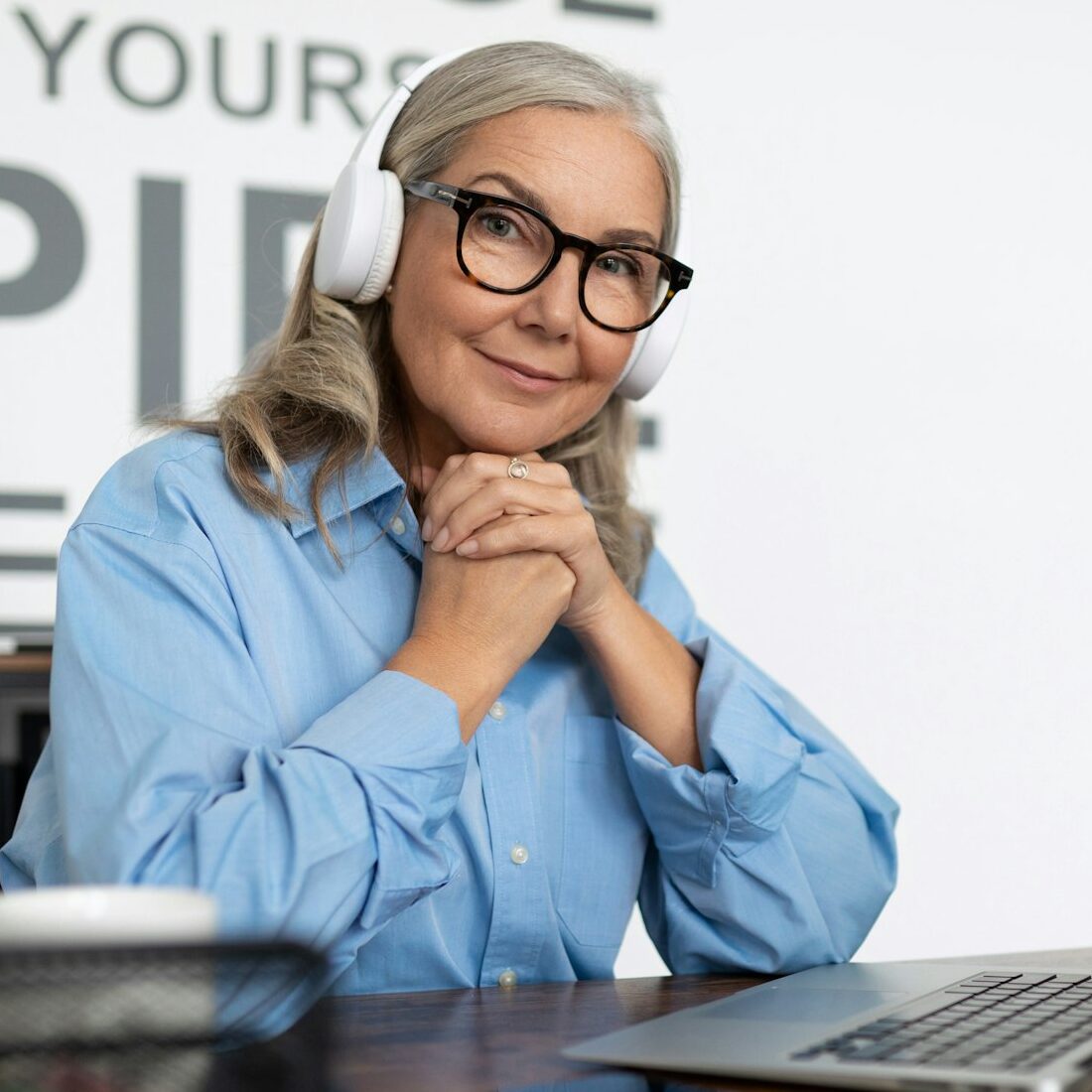 successful mature woman manager watching training video on laptop with headphones sitting at table